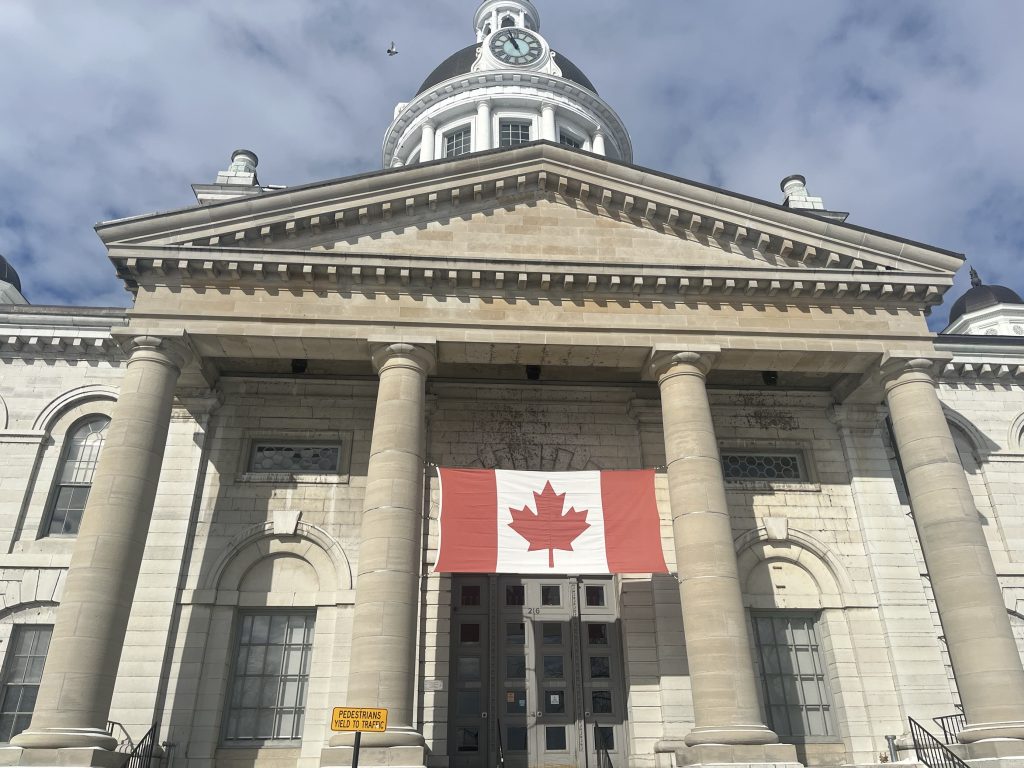 picture of Kingston City Hall with a large Canadian flag in front of it.