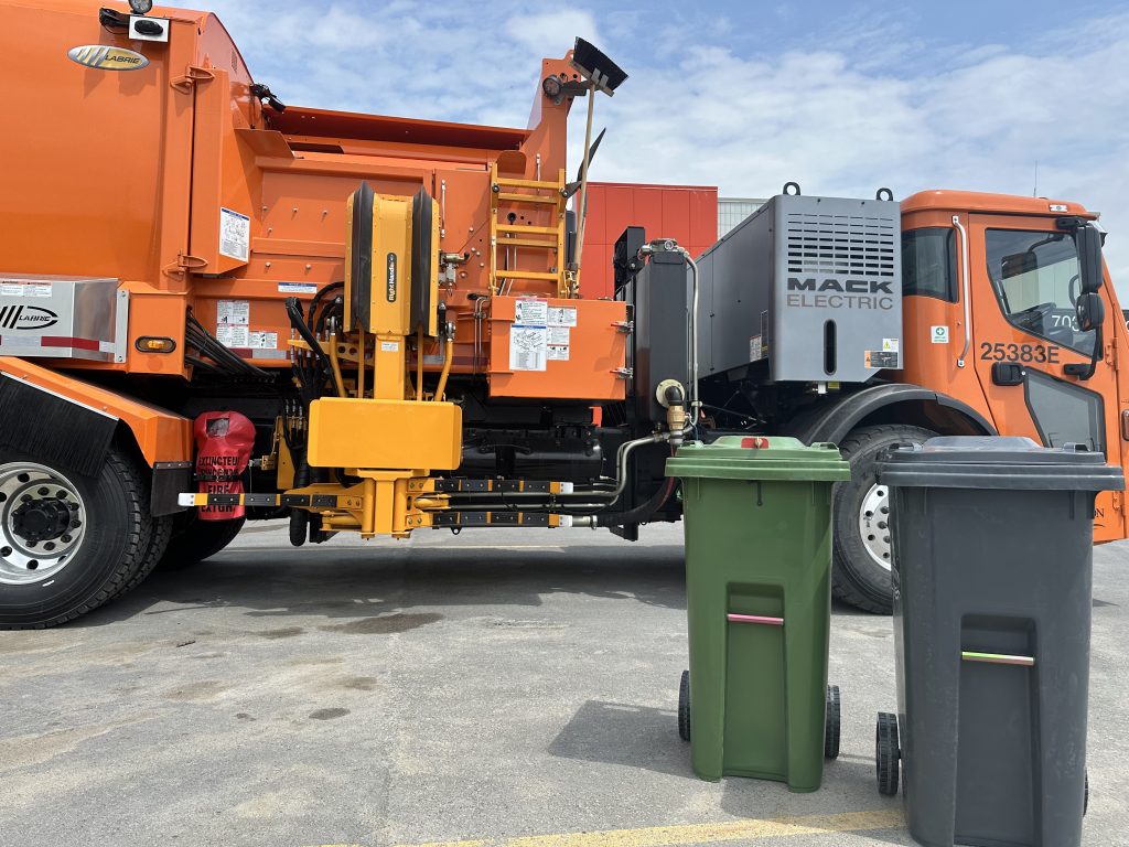 new automated garbage truck in the back. Two of the new garbage can can be seen at the front of the photos - a green one and a grey one.